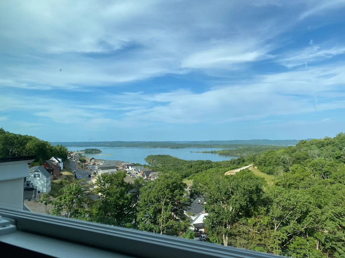A sweeping, elevated view of Table Rock Lake with lush greenery, scattered homes on the hillside, and the tranquil expanse of blue water capturing the region's natural beauty. The scene hints at outdoor adventures available nearby, such as boating, hiking, and lakeside relaxation.