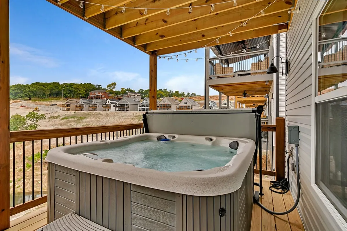 An inviting exterior patio scene showcasing a bubbling hot tub set on a wooden deck, draped in string lights, and surrounded by lush landscape with views—perfect for unwinding outdoors.