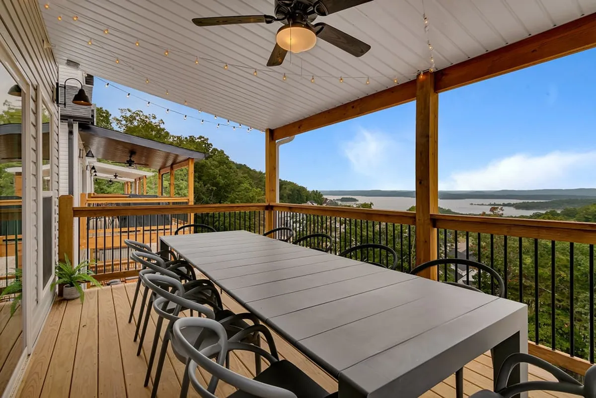 An expansive deck features a large dining table set for al fresco meals under string lights, with a stunning, uninterrupted view of Table Rock Lake in the background. The setting radiates a festive, welcoming vibe, perfect for outdoor gatherings and sunset toasts.