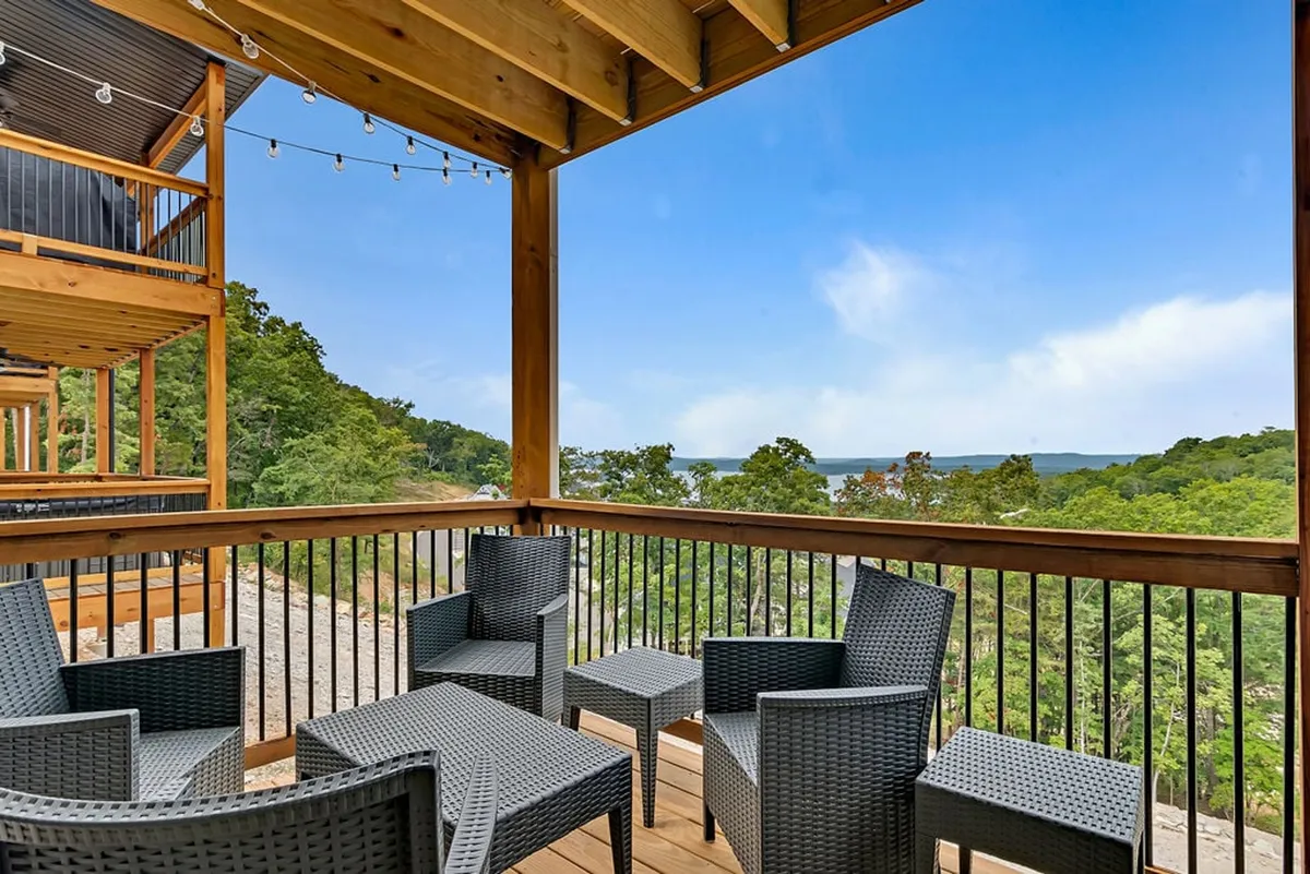 A spacious outdoor seating area overlooks a scenic landscape, with comfortable chairs arranged under glowing string lights. The setup suggests a perfect spot for relaxed socializing or dining al fresco while enjoying sunset or nighttime views over the lake.