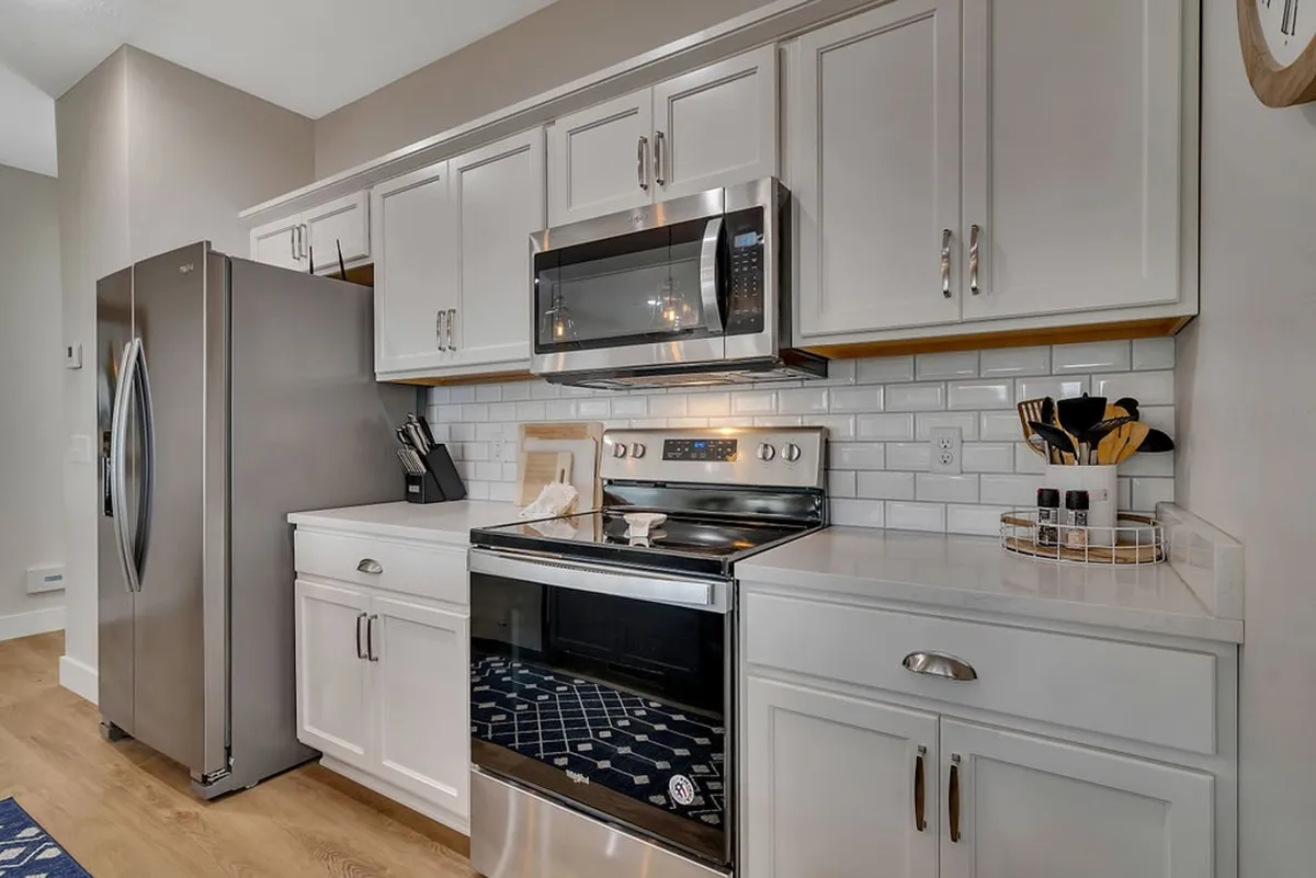 A modern, well-appointed bathroom with stainless steel appliances, white cabinetry, a crisp subway tile backsplash, and a blue decorative rug. The overall atmosphere is fresh, clean, and inviting.