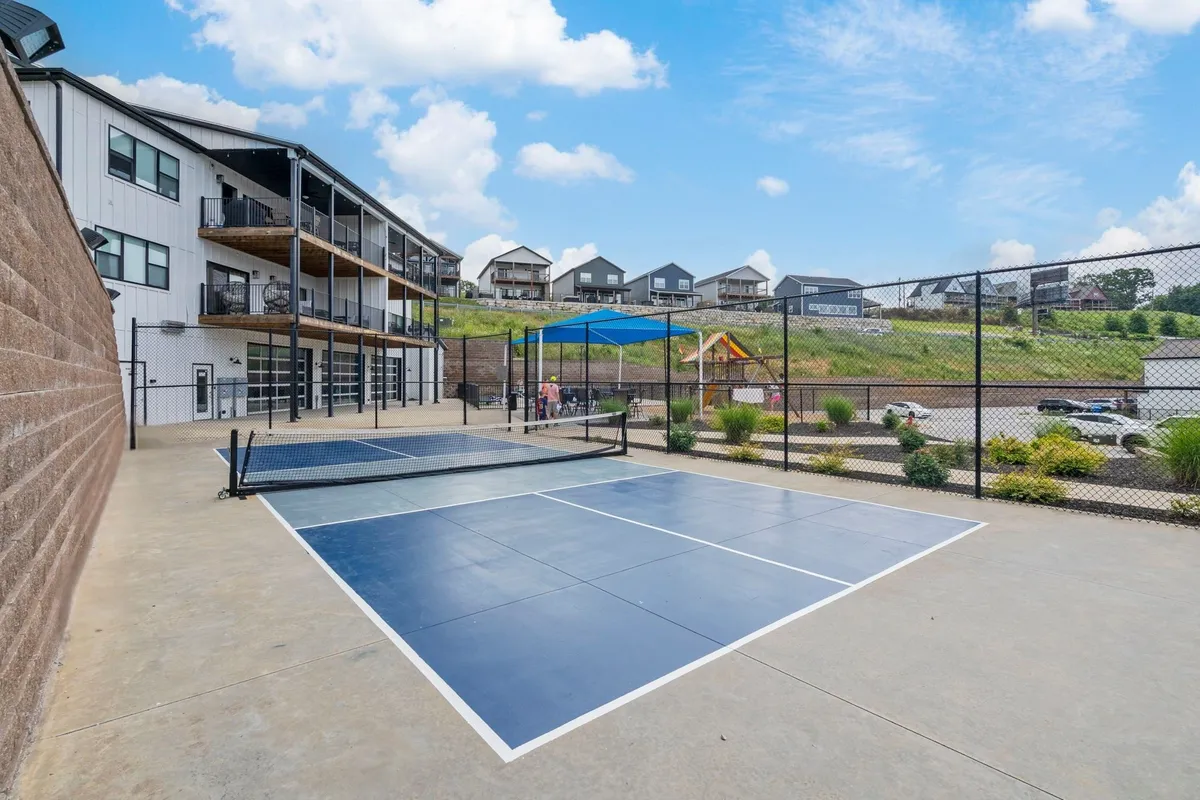 An exterior view of the multi-sport tennis court, a playground, and the balconies of nearby apartments. The area is lively and inviting, ideal for active pursuits and family-friendly gatherings.