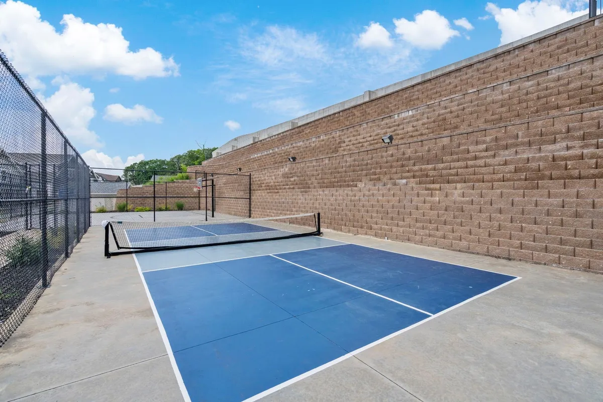 A vibrant exterior view of a pickleball court, surrounded by fencing and a textured wall. The court is clean and brightly colored, representing active recreation and community engagement.