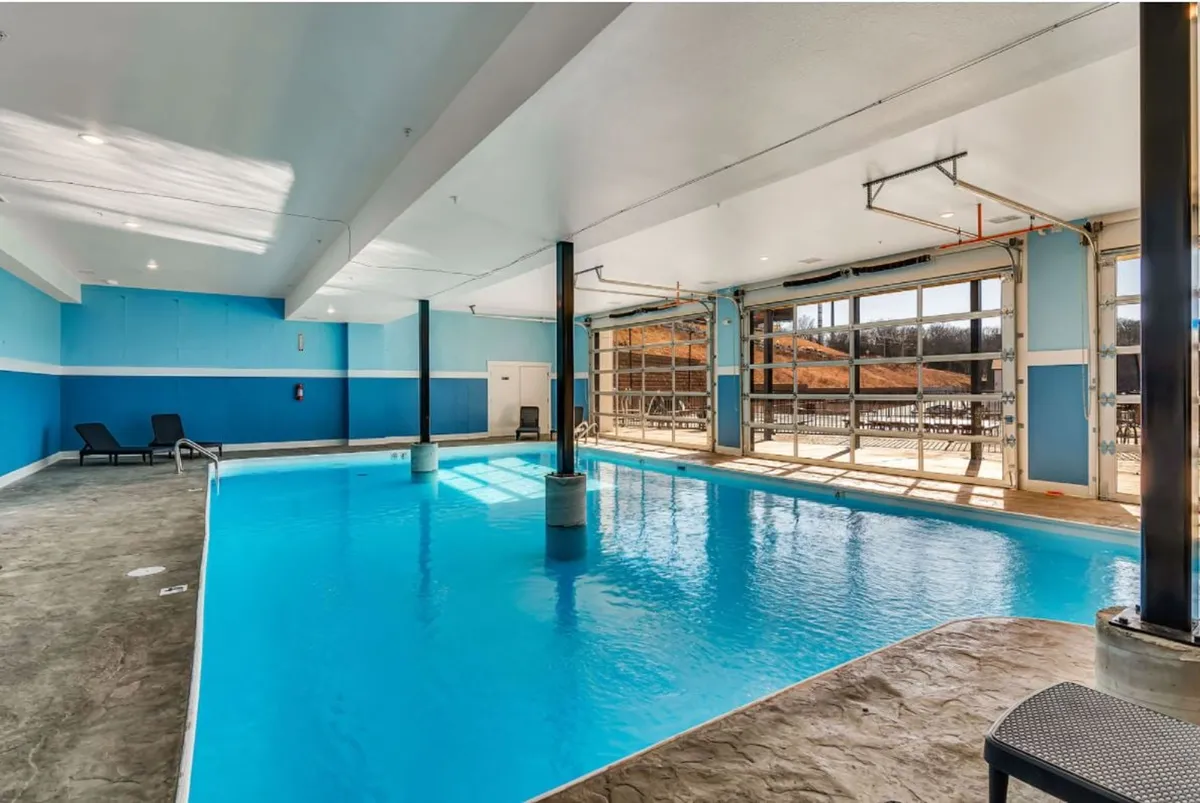 An inviting indoor swimming pool space with large windows that let in natural light, complemented by a comfortable seating area beside the pool. The atmosphere is relaxed and refreshing, perfect for year-round swims and social gatherings.